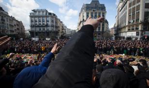 Masked and hooded men gesture outside the stock exchange in Brussels on March 27, 2016 as tensions mounted after the square was invaded by some 200 far-right football hooligans, during a tribute to the victims of the Brussels terror attacks. 